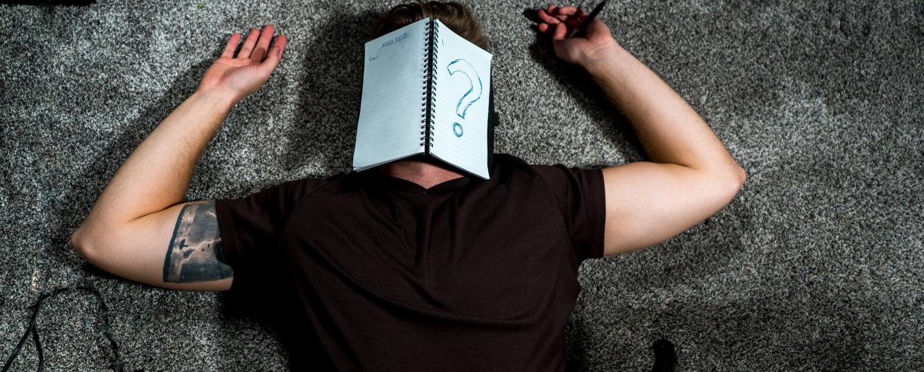 Man ligt op zijn rug met een notitieboekje op zijn gezicht