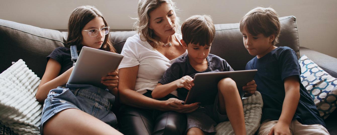 Een moeder die samen met haar kinderen op de zetel zit en met een tablet bezig zijn.